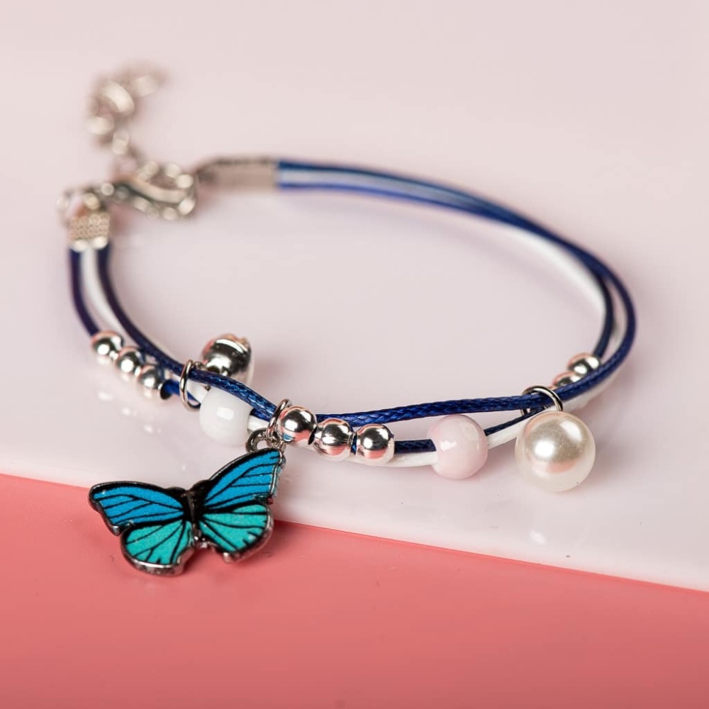 Armband mit blauem Schmetterlingsanhänger aus weißen Perlen auf weißem und rosa Hintergrund