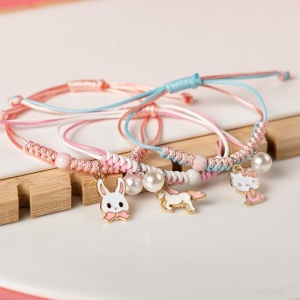 Geflochtenes Armband mit Perlenanhänger und rosa und blauem Tier auf weißem Hintergrund und Holz