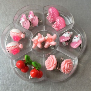 Set aus 7 Clip-Ohrringen für Kinder in Rosa, in einem transparenten Teiler mit weißem Hintergrund