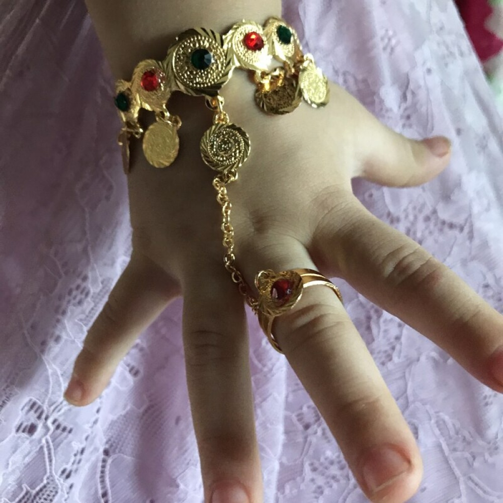 Armband und Ring, verbunden durch eine Kette, für ein kleines Mädchen an einer Kinderhand mit einem weißen Rock