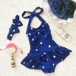 Einteiliger Badeanzug für Mädchen mit blauer Augenbinde mit weißen Punkten und einer Puppe nebenan auf einem weißen Teppich