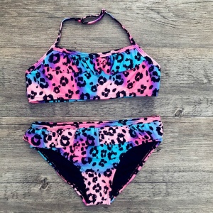 Zweiteiliger Badeanzug mit Leopardenmuster für Mädchen in rosa, lila und blau auf grauem Holz