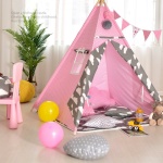 Tipi mit kleinen weißen und rosa Punkten für Kinder in einem Zimmer mit einer grünen Pflanze und Ballons auf dem Boden, mit einem rosa Stuhl
