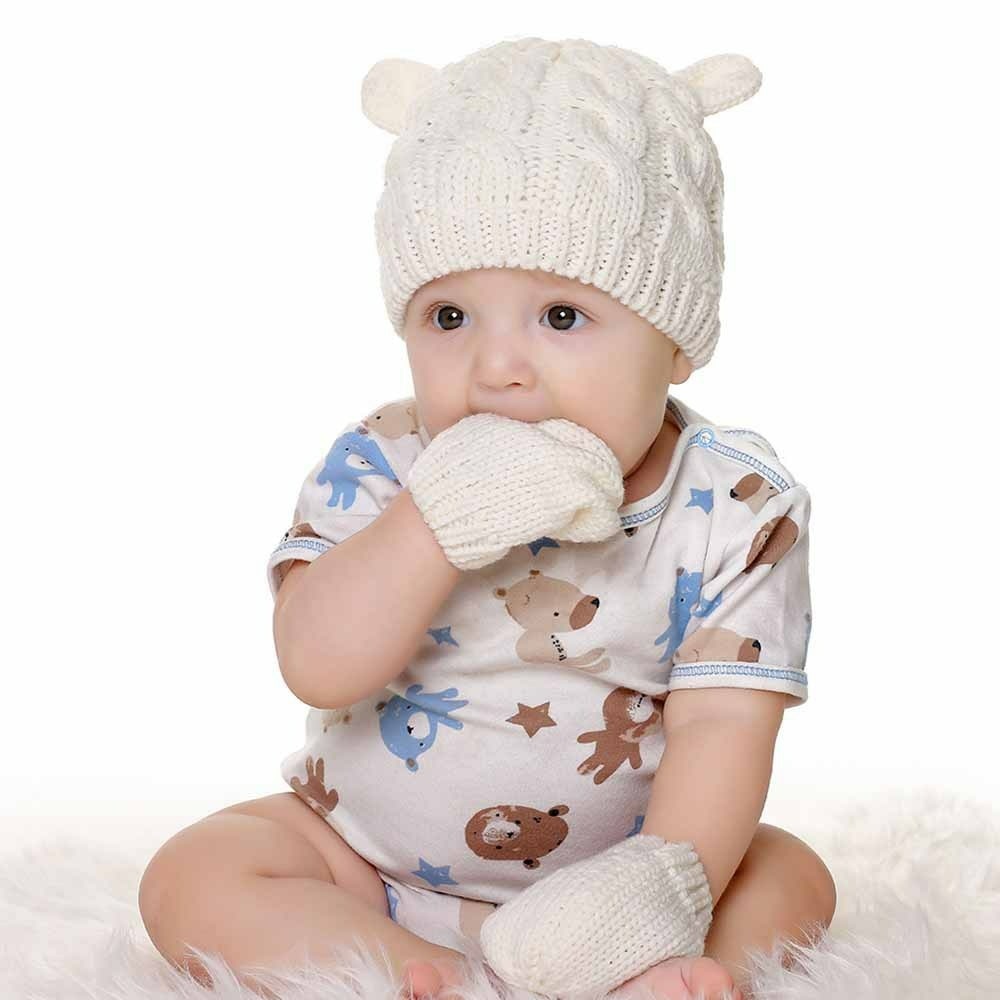 Set aus Wintermütze und Fäustlingen für Babys in Weiß mit Baby mit Hand im Mund und weißer Kleidung mit Muster