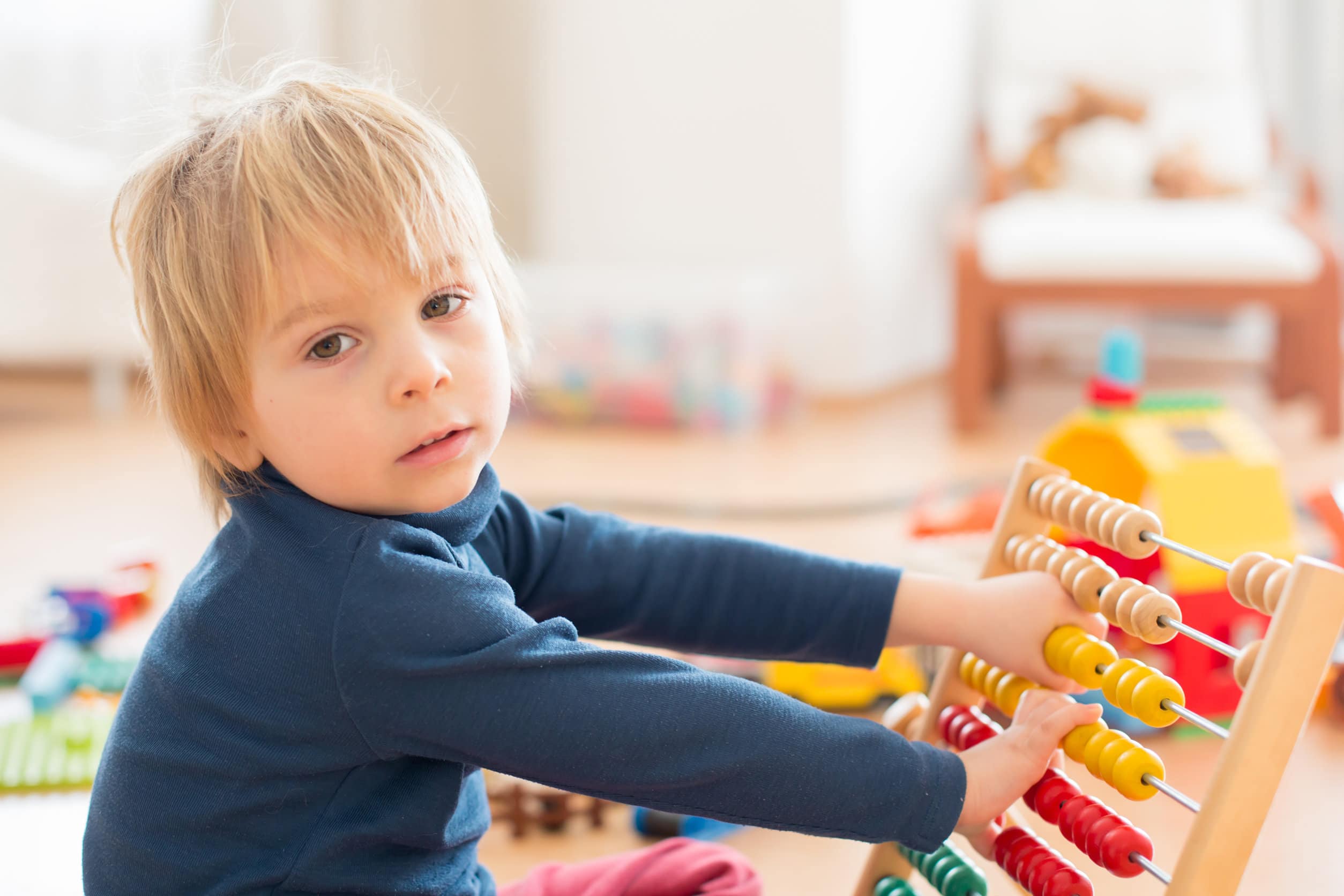 Ein Junge mit halblangen blonden Haaren und einem blauen Pullover, der mit einem farbigen Abakus spielt, um das Zählen zu lernen