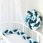 Blau-weißer geflochtener Bettumrandung auf einem weißen Babybett und einer weißen Wand mit weißer Bettwäsche