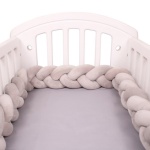 Grau geflochtener Bettumrandung in einem weißen Babybett und grauer Bettwäsche