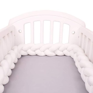 Weißer geflochtener Bettumrandung in einem weißen Babybett mit grauer Bettwäsche