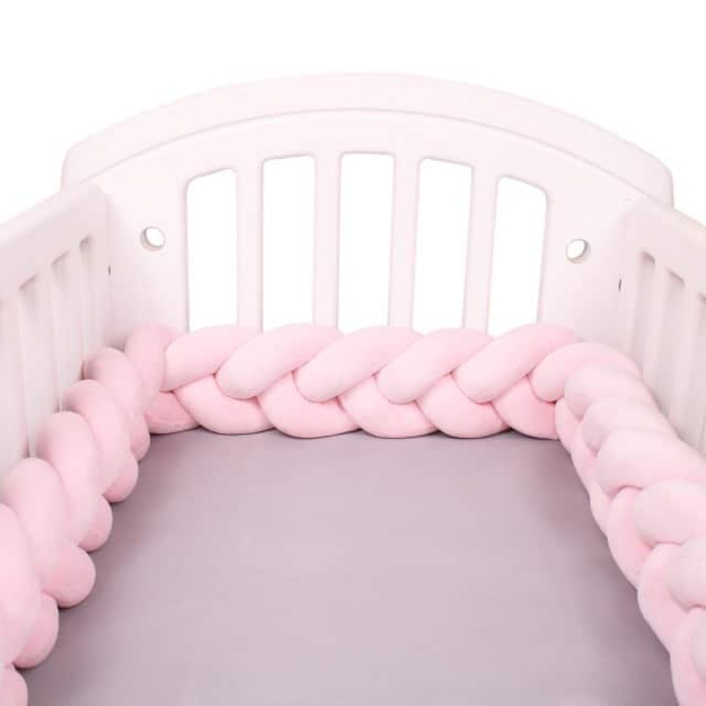 Bettumrandung aus rosa Zopf in einem weißen Babybett mit grauer Bettwäsche