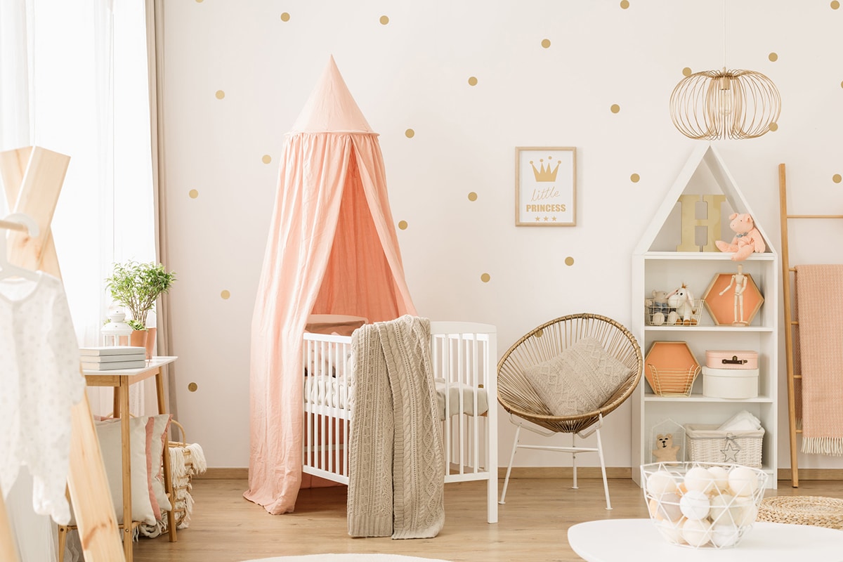 Ein aufgeräumtes Kinderzimmer. Die Farbtöne sind rosa, es gibt ein Babybett, Aufbewahrungsmöbel und Dekorationen.