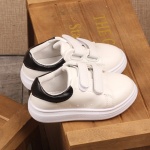 Flache, lässige Sneakers für Kinder in Weiß mit Schnürsenkeln auf einem Holzstuhl