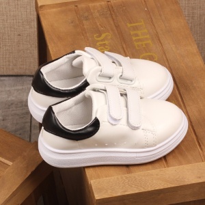 Flache, lässige Sneakers für Kinder in Weiß mit Schnürsenkeln auf einem Holzstuhl