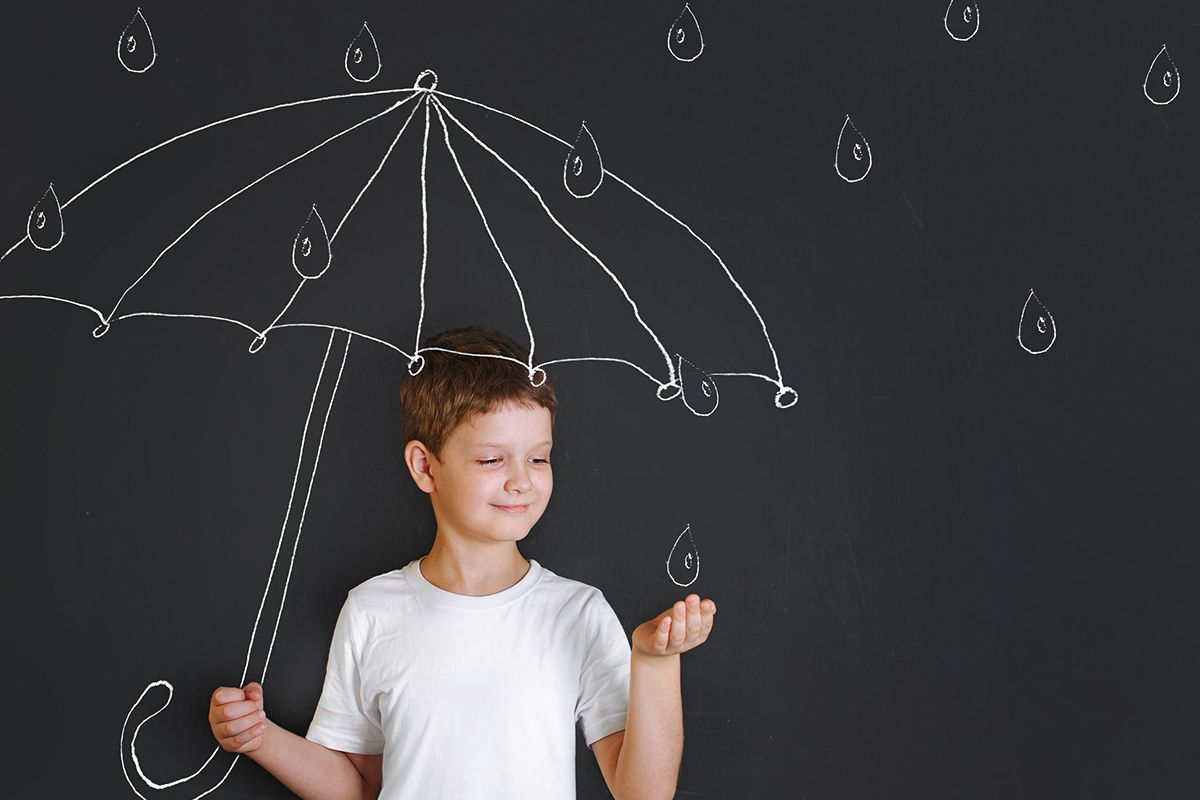 Ein Junge in einem weißen T-Shirt, der vor einem Gemälde steht, auf dem ein Kinderregenschirm und Regentropfen abgebildet sind