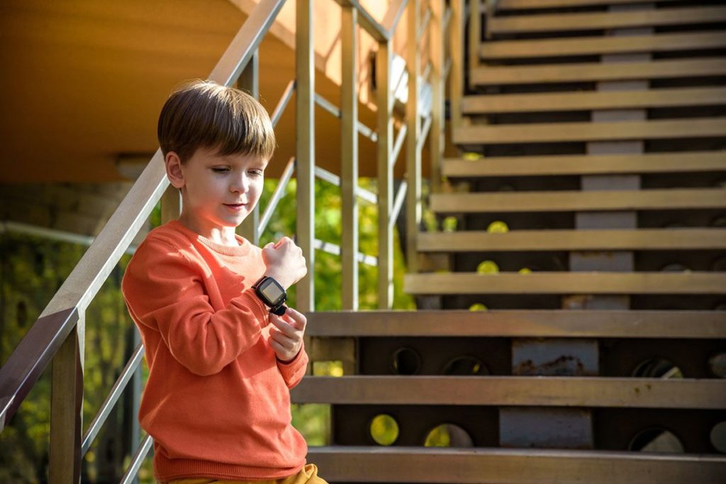 Un jeune garçon en bas des escaliers. Il porte une smartwach noire et appuie dessus.