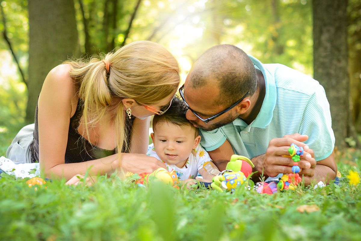 Eine fröhliche Familie liegt im Gras. In der Mitte befinden sich die Mutter, der Vater und ihr Baby.