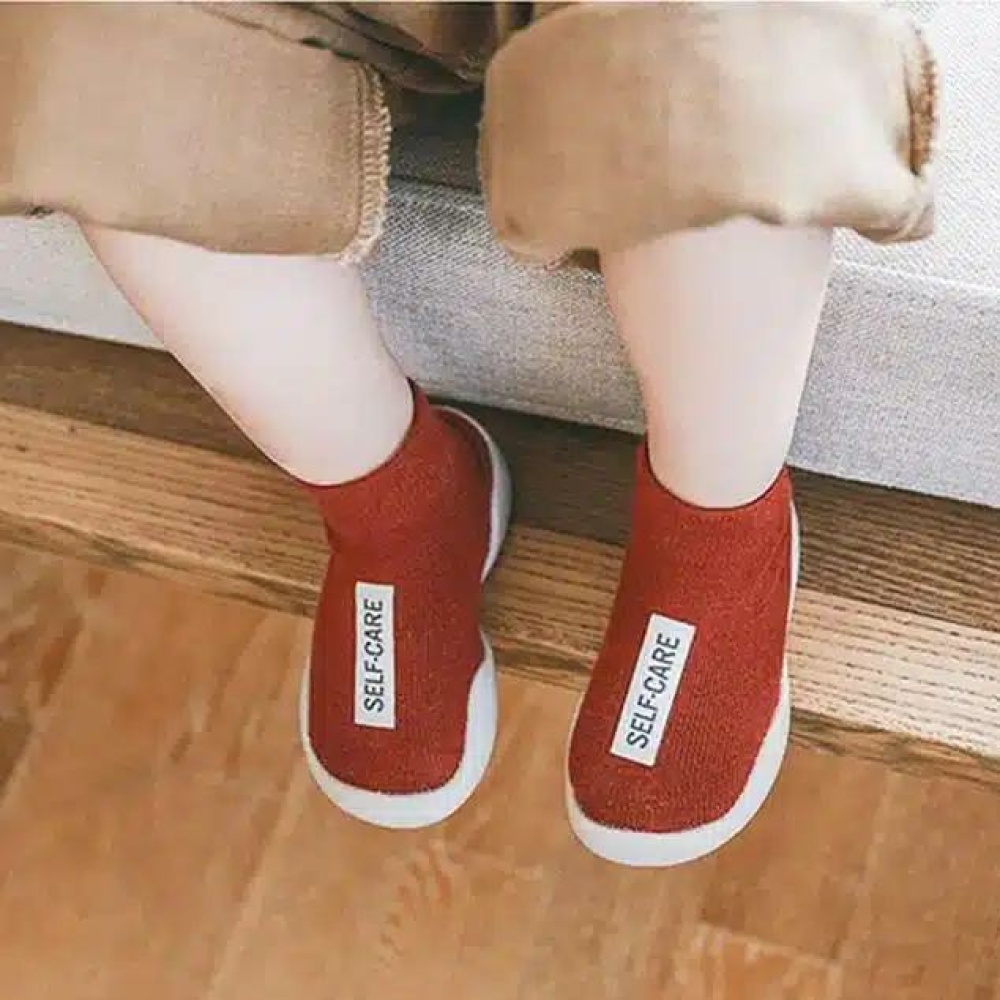 sie sehen die Beine eines sitzenden Kindes, das rote Sockenschuhe mit einem weißen Etikett trägt