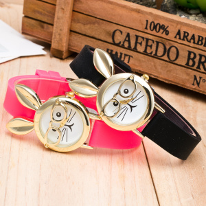 auf einem Holztisch liegen zwei Uhren des gleichen Modells, neben einer Holzkiste, eine rosa und eine schwarze, auf dem Zifferblatt ist ein niedliches Kaninchen mit Brille abgebildet