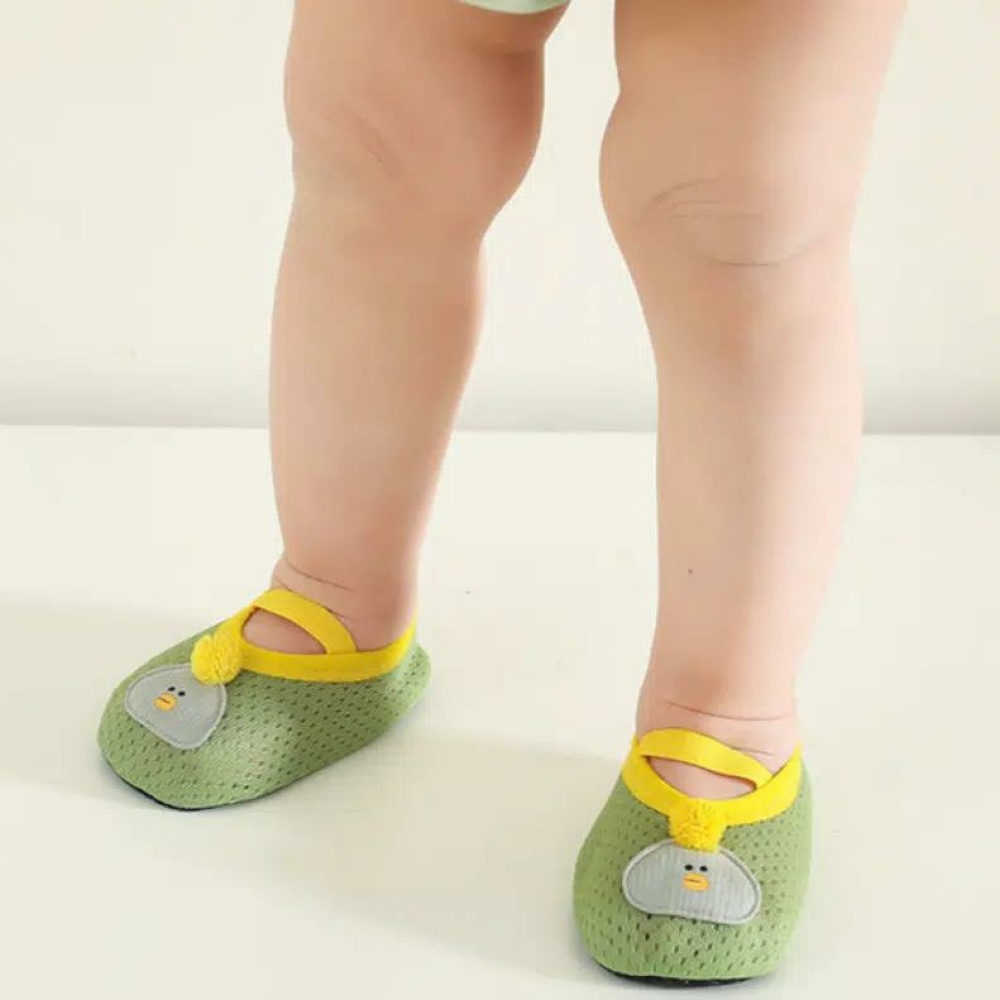 ein Baby steht und man sieht nur seine Beine, es trägt kleine, weiche und atmungsaktive grüne Schühchen