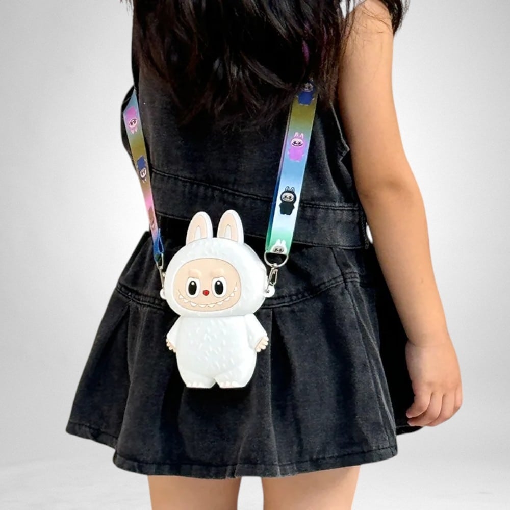 IMG_1000X1000_sac_enfant_petit_monstre_labubu10.jpg Mädchen mit einer kleinen weißen Silikontasche in Form eines Labubu-Monsters mit Hasenohren und farbigem Schulterriemen.
